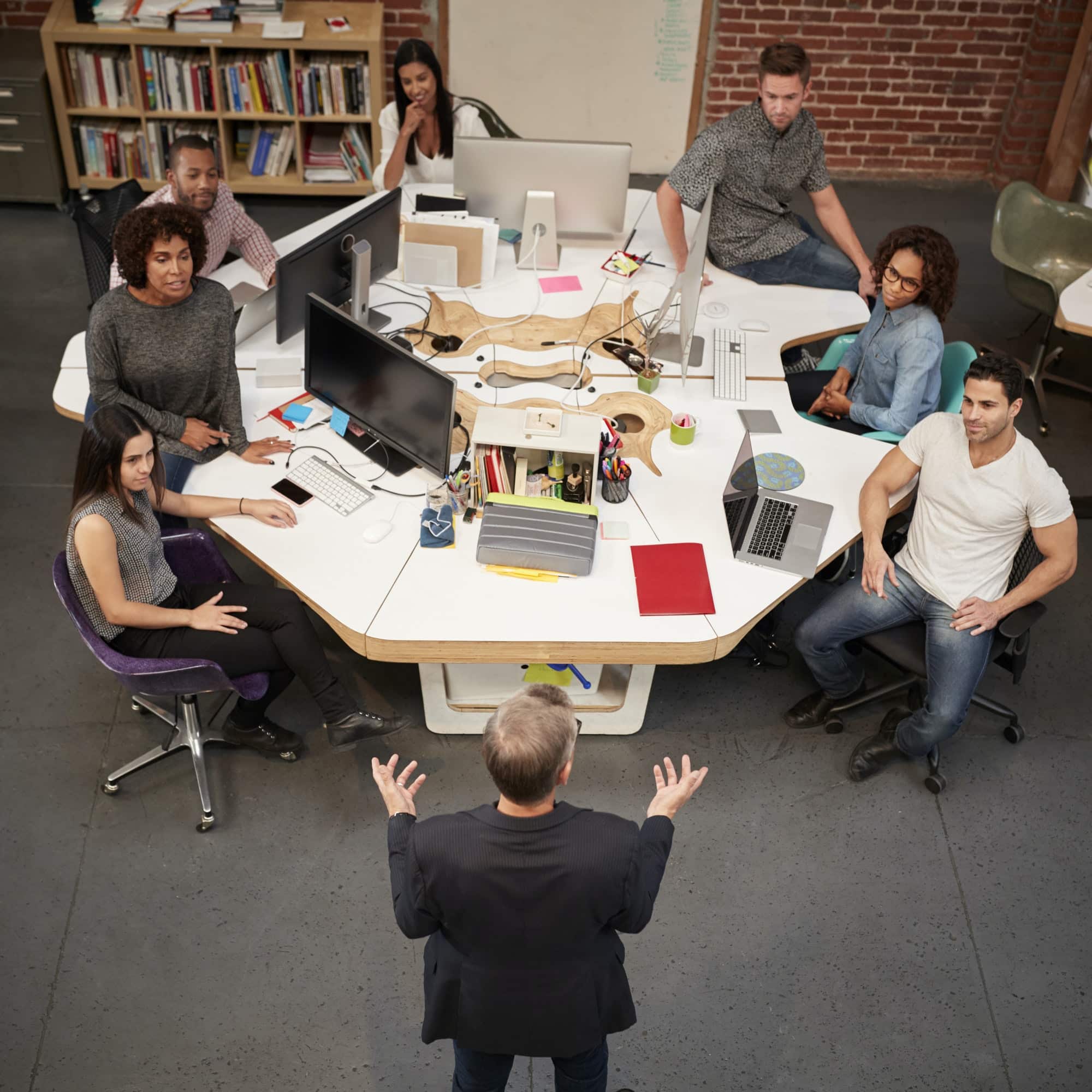 Senior Businessman Talking At Meeting Of Casually Dressed Business Team In Open Plan Office